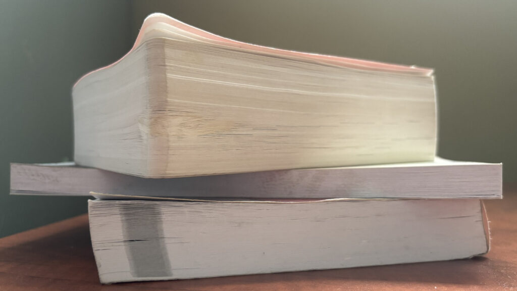 Three books are stacked on top of each other on a wooden desk.